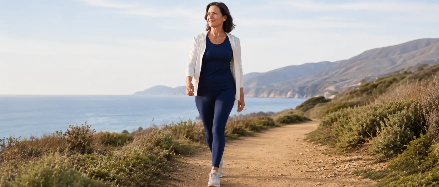A woman walking confidently along a coastal path — representing the daily consistency that protects mobility and joint health for women in midlife