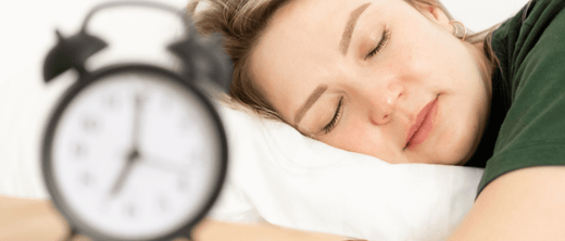 A woman sleeping next to an alarm clock, symbolizing restful sleep and its role in reducing inflammation.