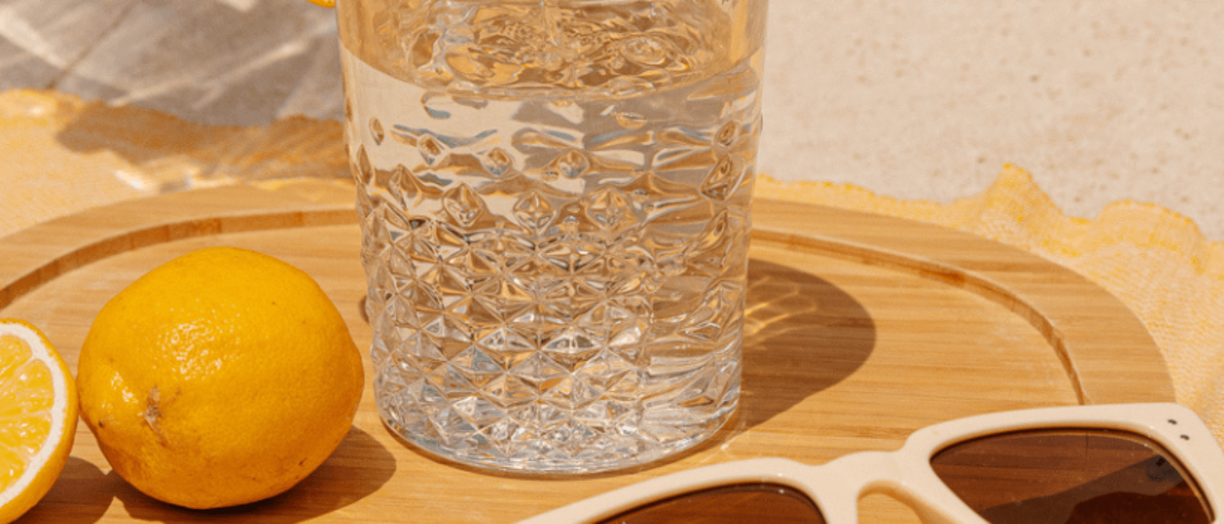 Glass of water with lemon on a wooden table in summer light