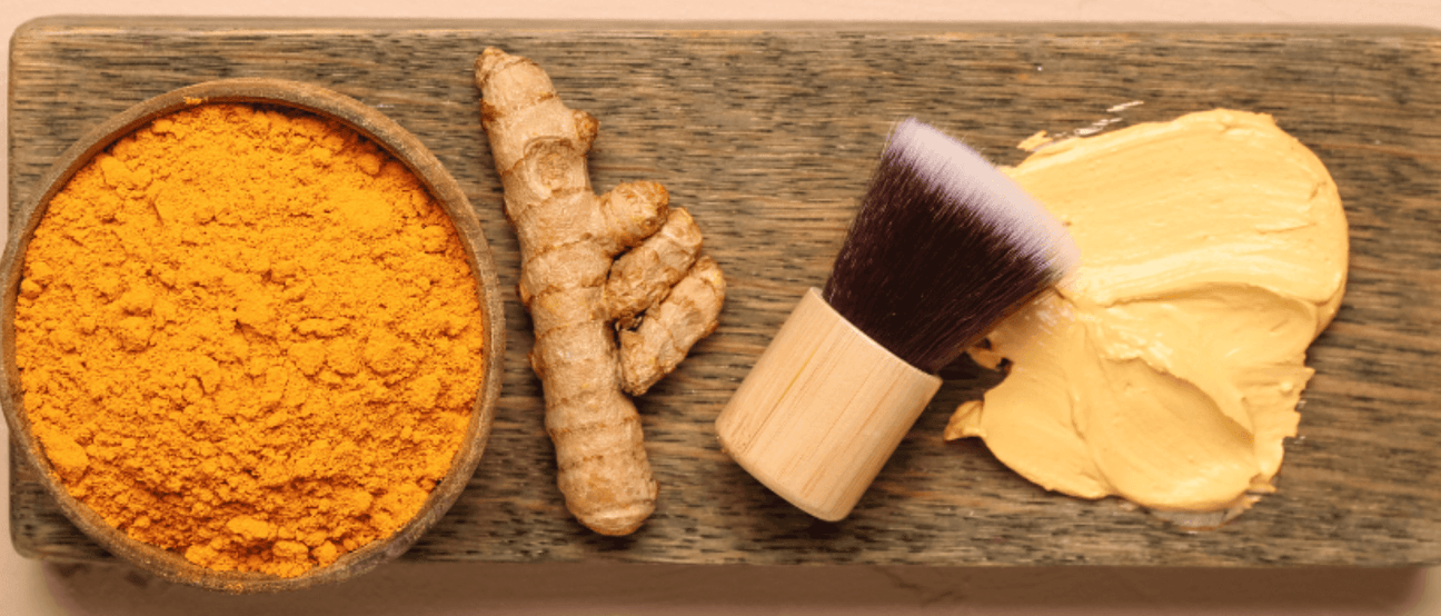 Turmeric roots and powder with skincare brush for natural anti-aging treatments.