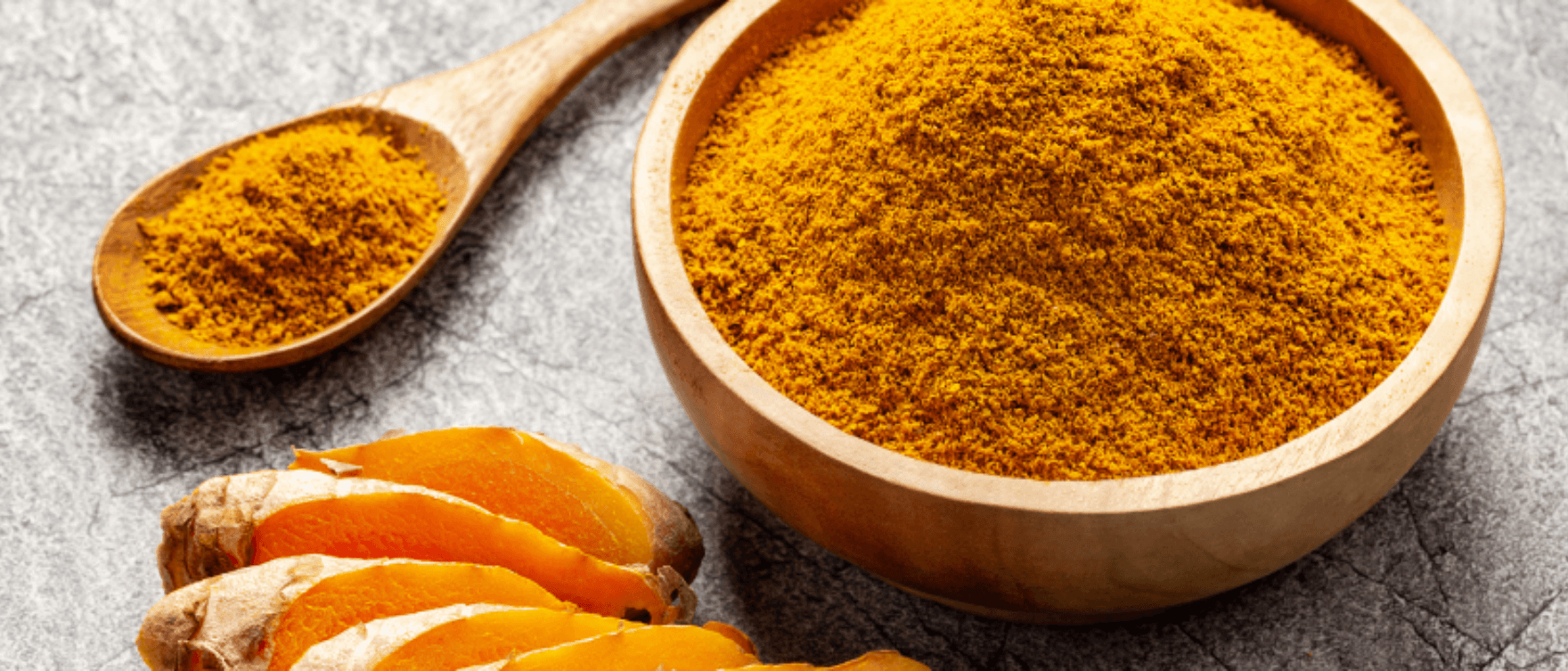 Turmeric powder in a wooden bowl with fresh turmeric roots.